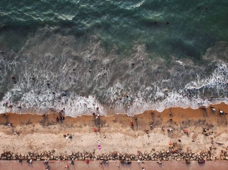 From above aerial view of beach with people spending weekend on ocean coastline