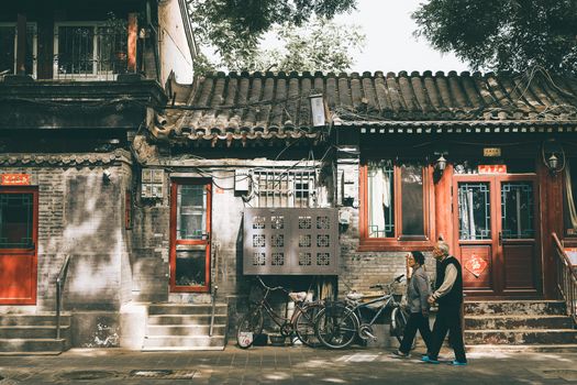 一对老夫妇漫步在一条传统的北京胡同里，胡同两旁是复古建筑和红门