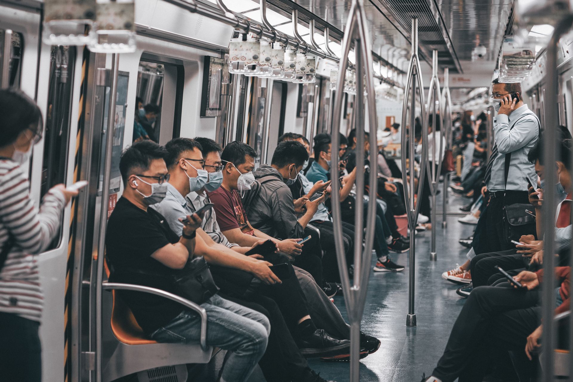 People wearing masks and using phones on Beijing subway train, showcasing urban life during pandemic.