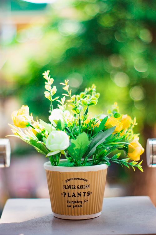 Free Vibrant artificial flowers in decorative pot with blurred background, perfect for home decor. Stock Photo