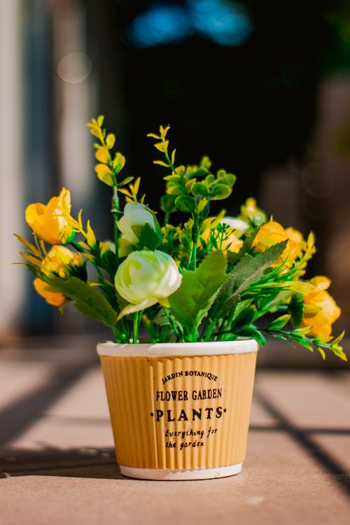 Free Colorful artificial flowers in a labeled pot with a blurred background, captured in natural light. Stock Photo