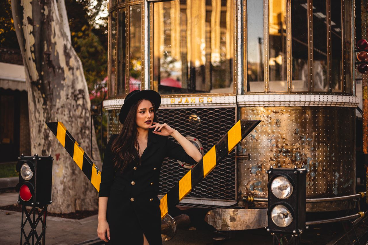 stylish woman in a black outfit posing near a vintage tram in an urban