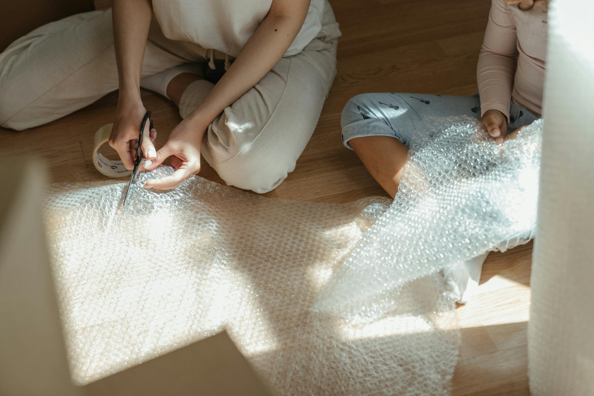A mother and daughter sit on the floor cutting bubble wrap for moving.