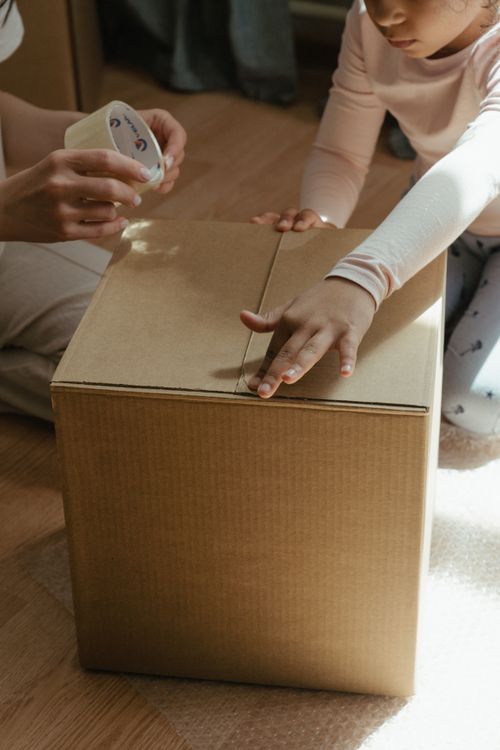 Free A mother and child sealing a cardboard box while relocating indoors. Stock Photo
