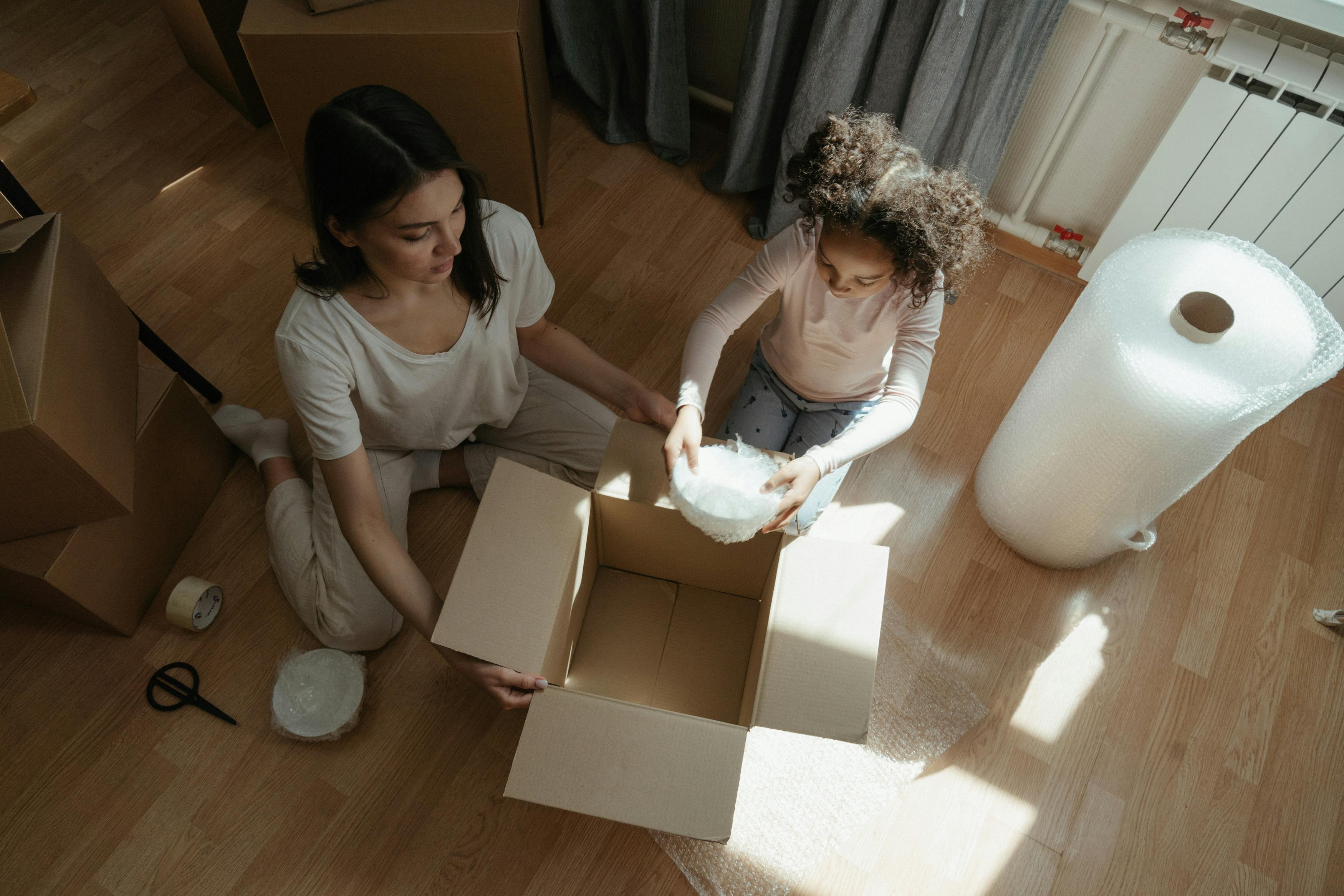 woman in gray shirt sitting on floor beside girl in white shirt