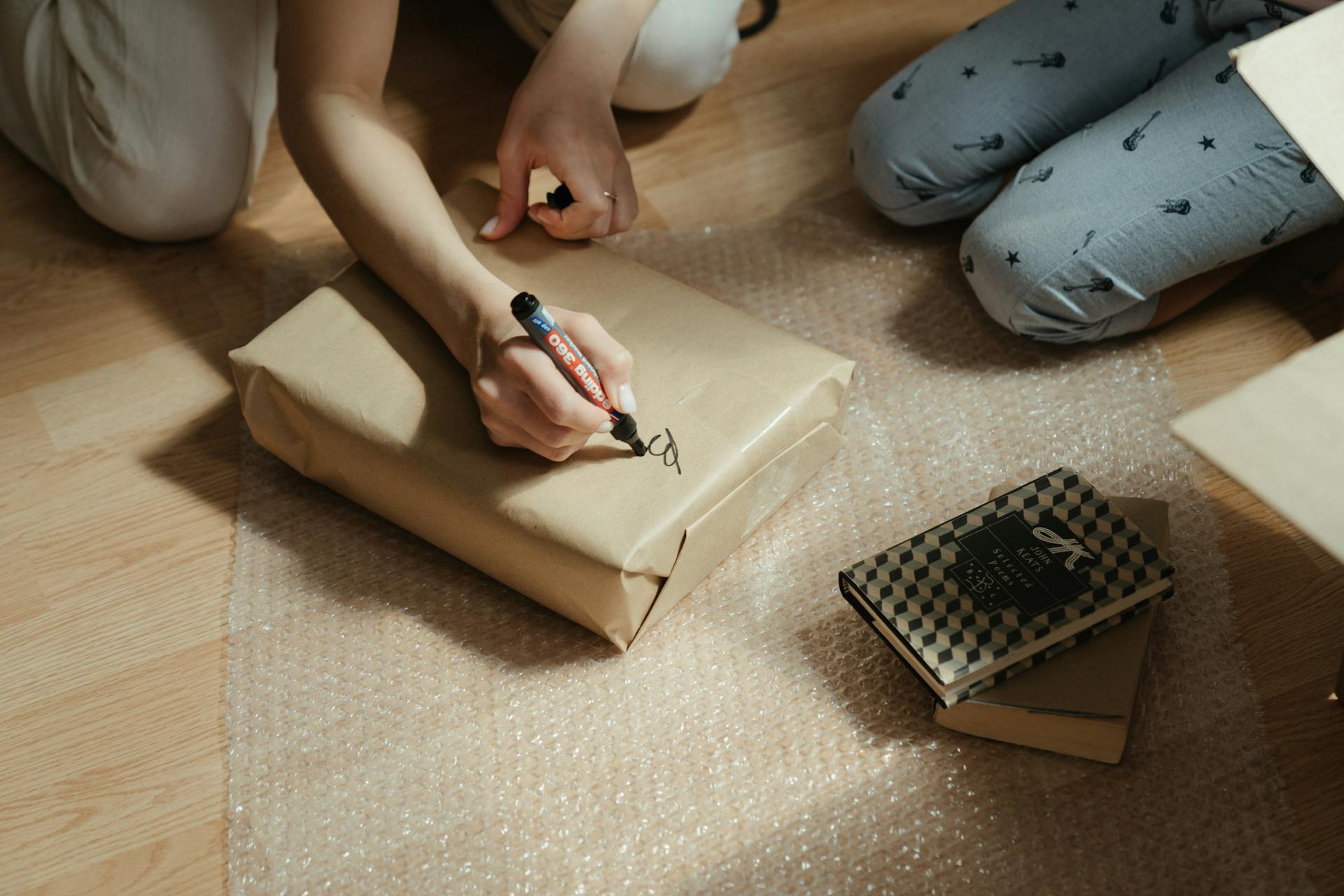 Hands writing on a wrapped package, preparing books with bubble wrap for secure shipping.