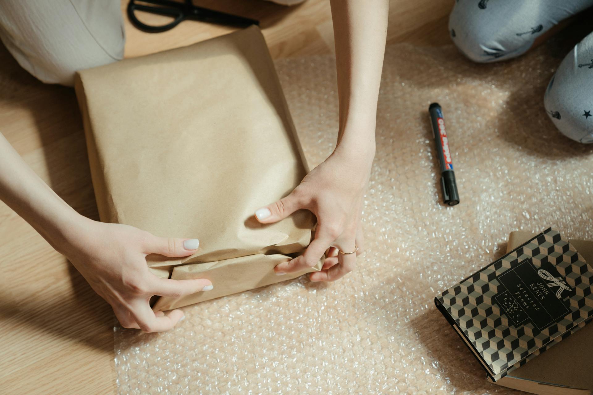 Close-up of hands wrapping a package with brown craft paper on bubble wrap surface.