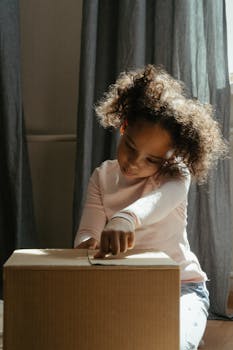 A joyful child with curly hair excitedly unpacks a cardboard box inside a cozy apartment.