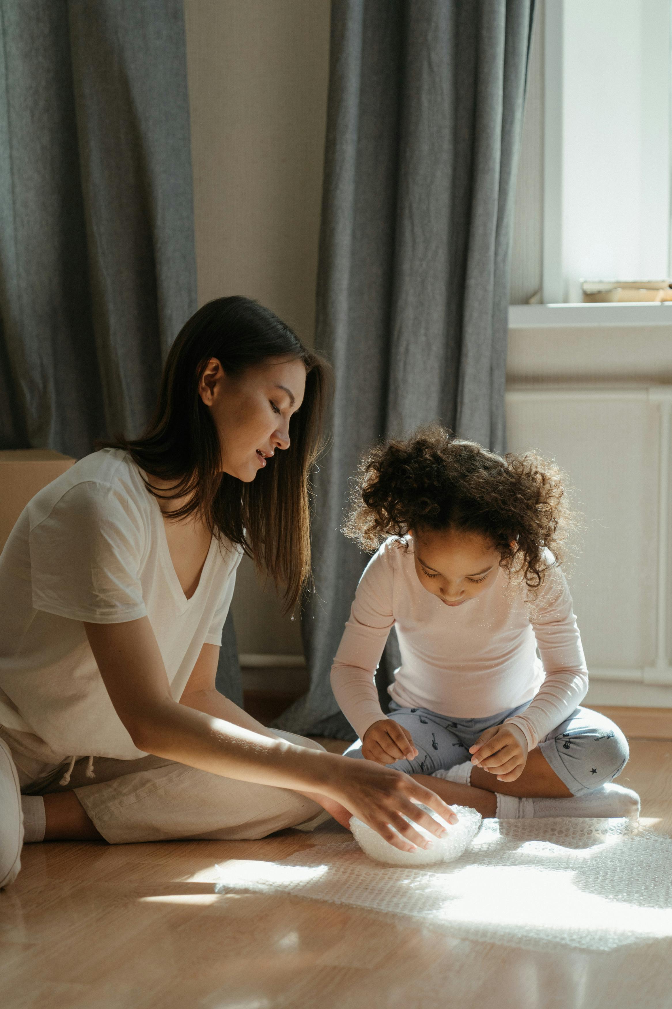 一对母女在家坐在地板上，裹着气泡纸