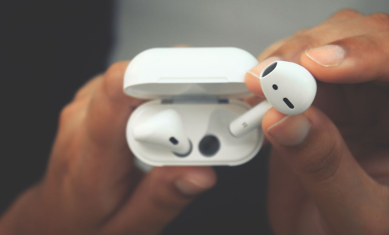Hands holding wireless earbuds in an open charging case