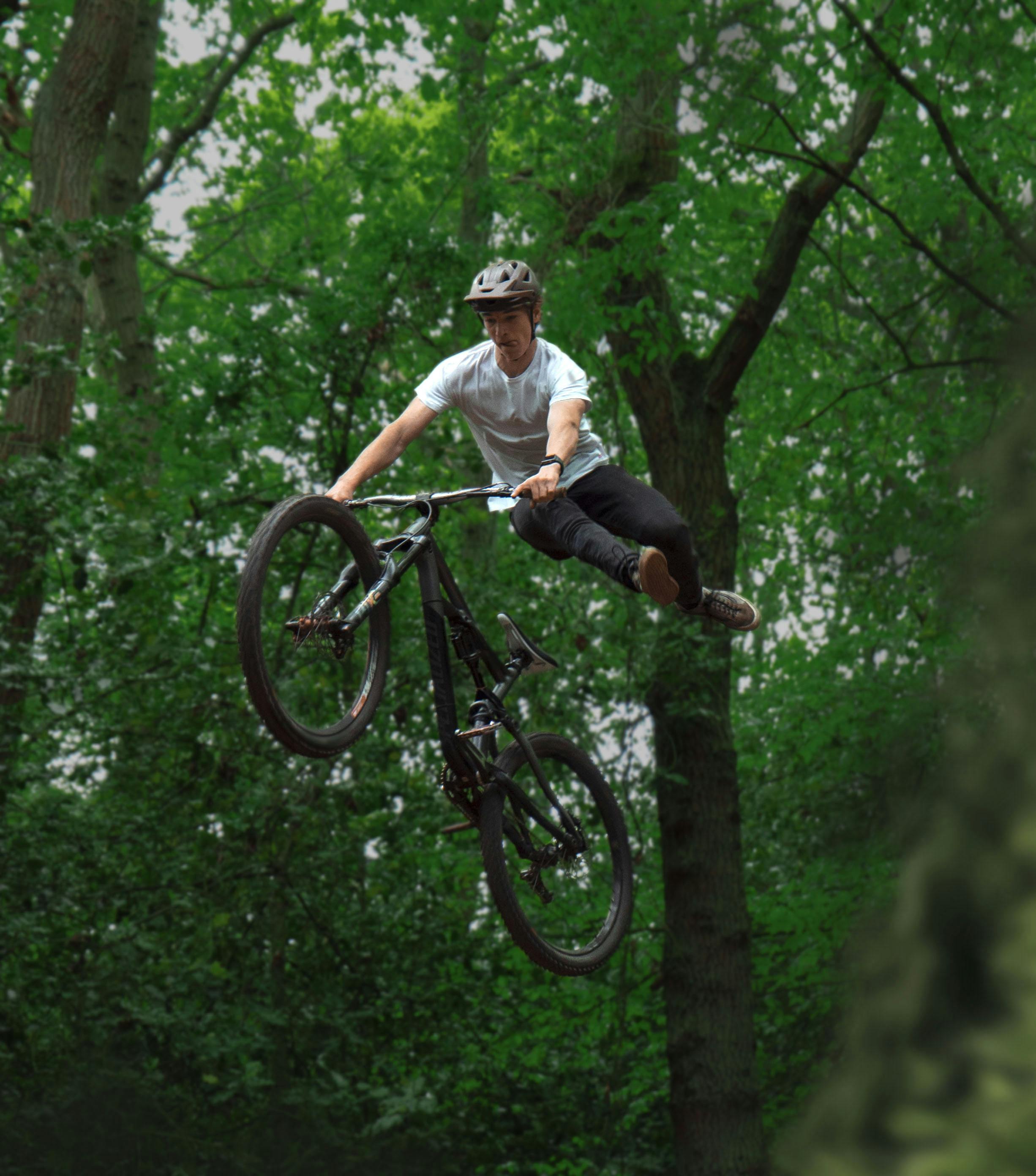 Mountain biker performs a thrilling stunt in a lush green forest.