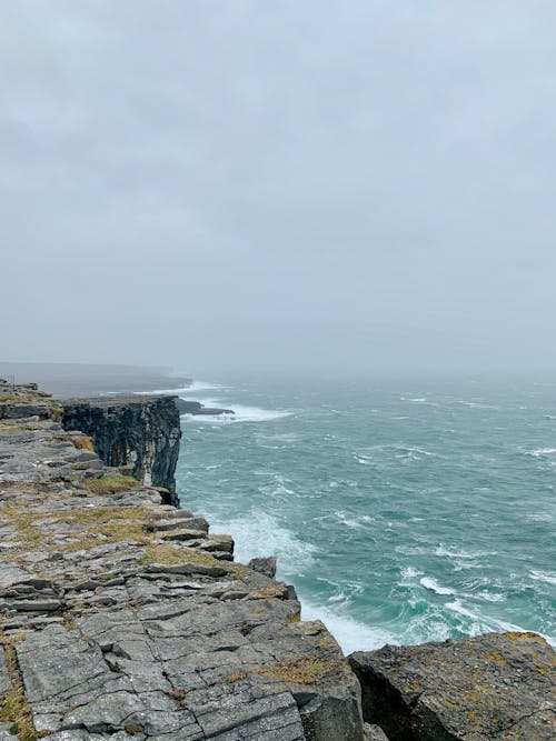 Misty cloudy sky over powerful stormy ocean with waves crashing against huge rocky cliffs