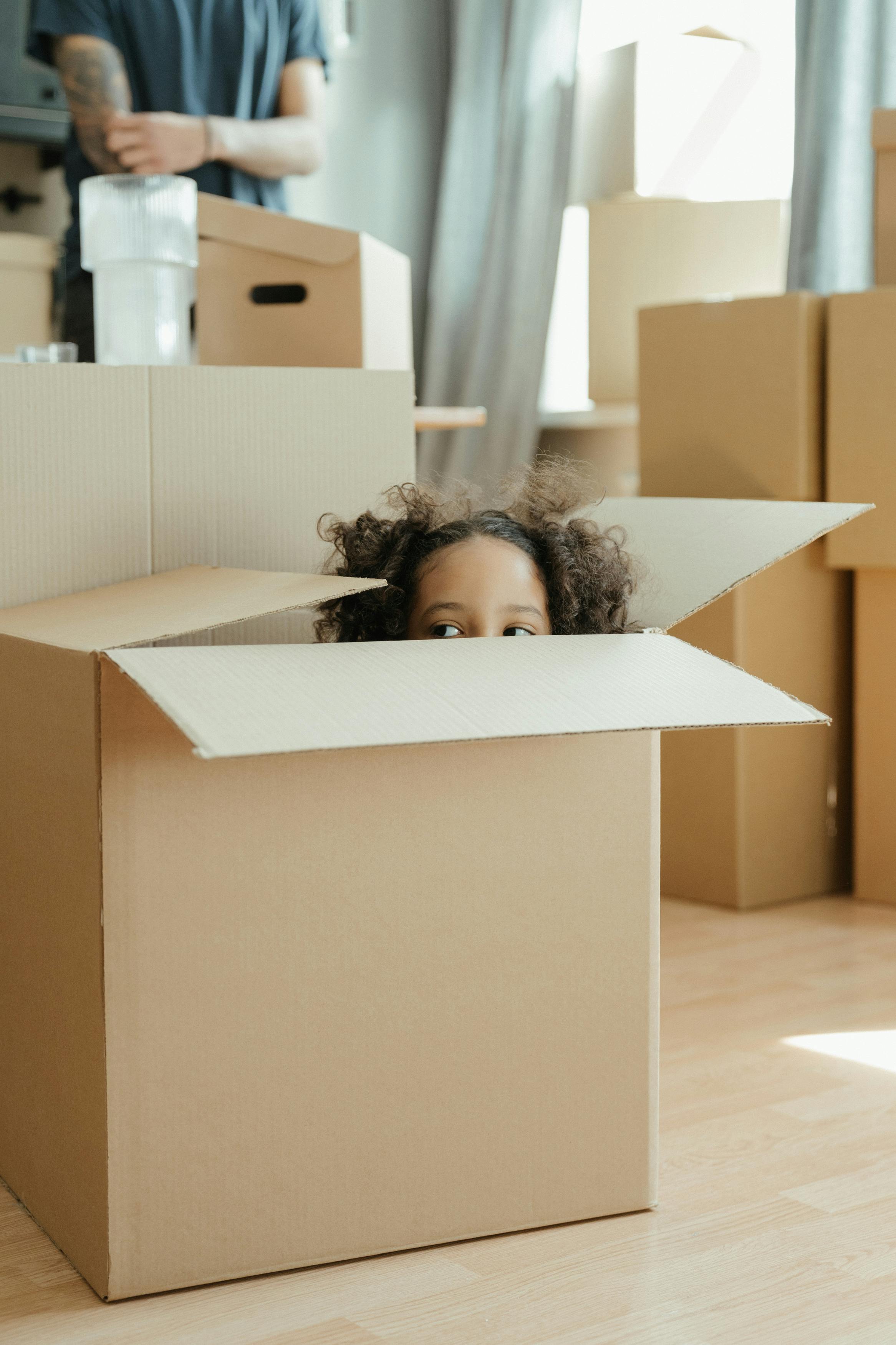 Cute little girl playing in a box while helping the family move