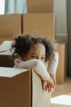 可爱的卷发孩子，在搬家的日子里从纸板箱里偷看