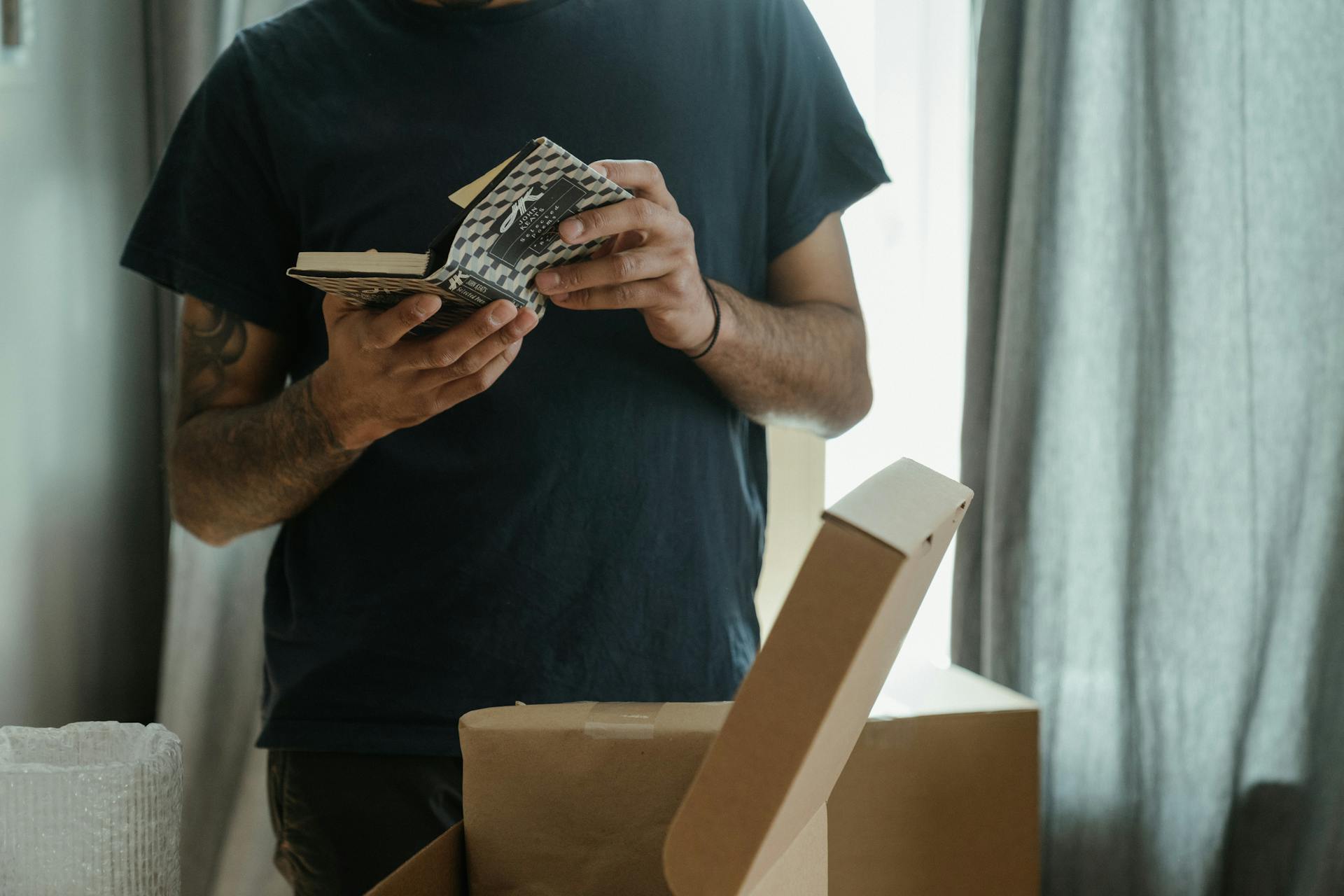 A man unpacks boxes in a new home, holding a small book, symbolizing a fresh start.