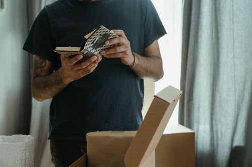 Free A man unpacks boxes in a new home, holding a small book, symbolizing a fresh start. Stock Photo