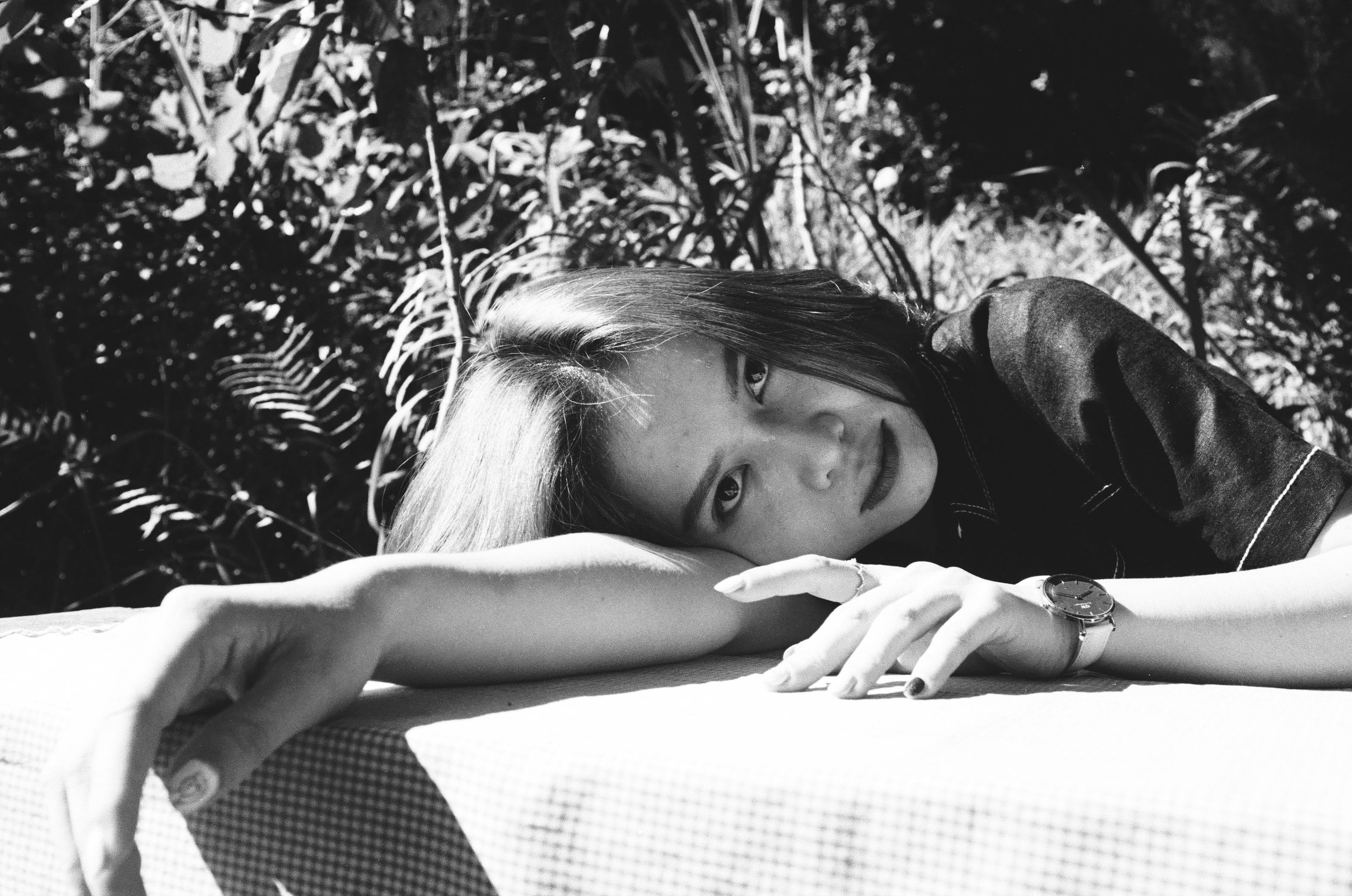 Monochrome photo of a woman resting on a table outdoors, thoughtful expression.