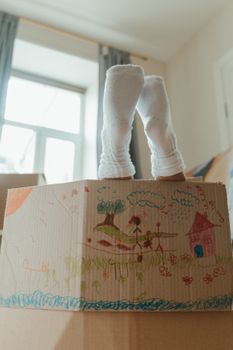 室内，一个穿着袜子的孩子从装饰好的纸板箱里向外张望
