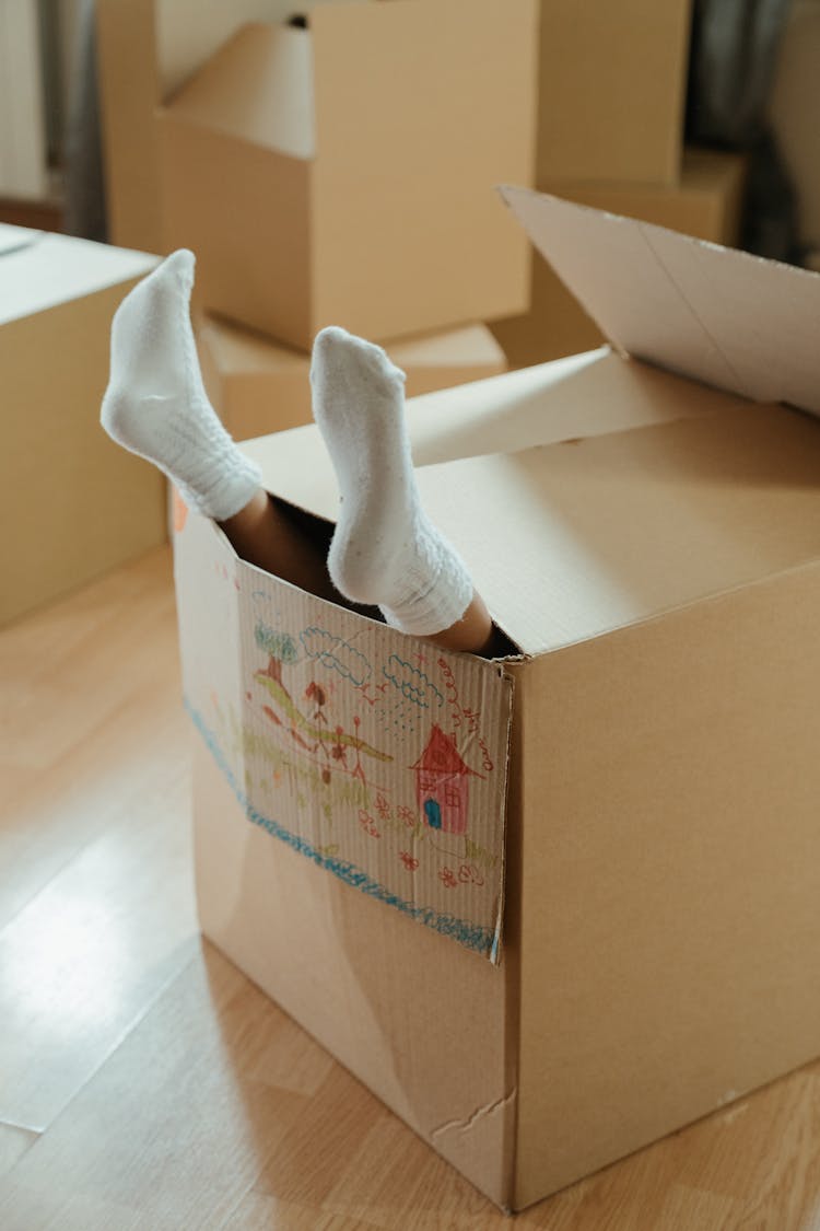 Person Wearing White Socks On Brown Cardboard Box