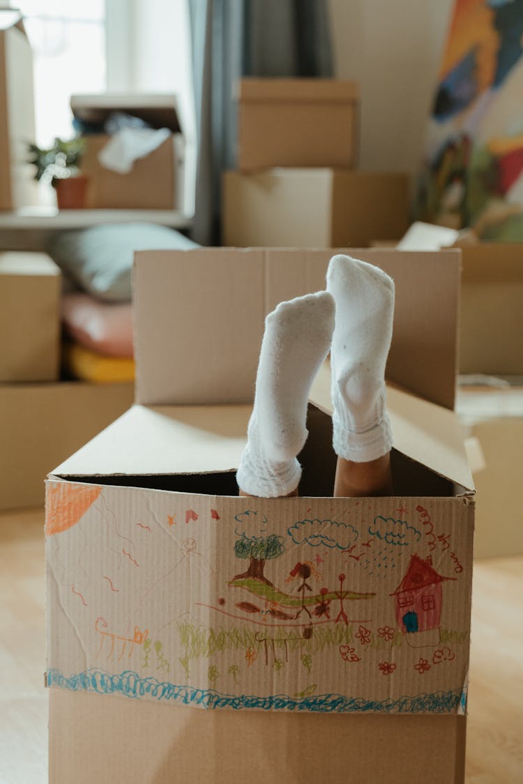 Person In White Socks Standing On Brown Cardboard Box