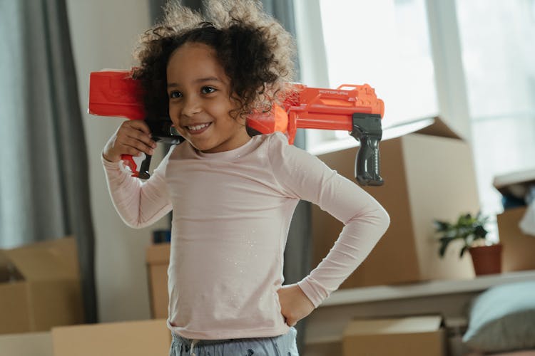 Girl In White Long Sleeve Shirt Holding Red Plastic Toy Gun