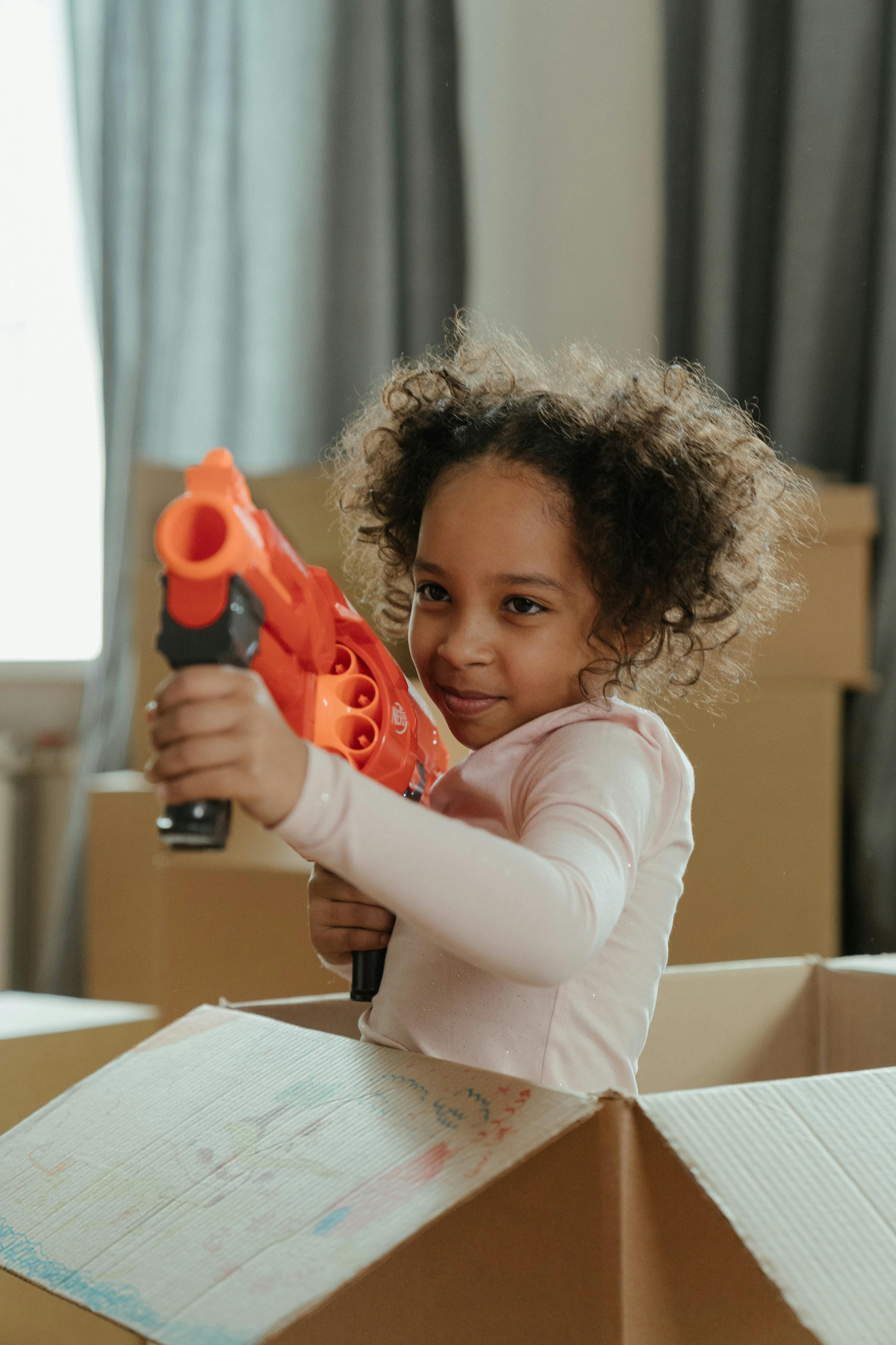 child in white long sleeve shirt holding orange and black toy gun