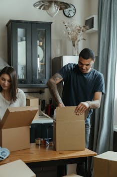 A couple unpacking cardboard boxes in their kitchen, settling into a new home.