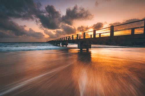Footbridge over sandy beach of sea at sundown