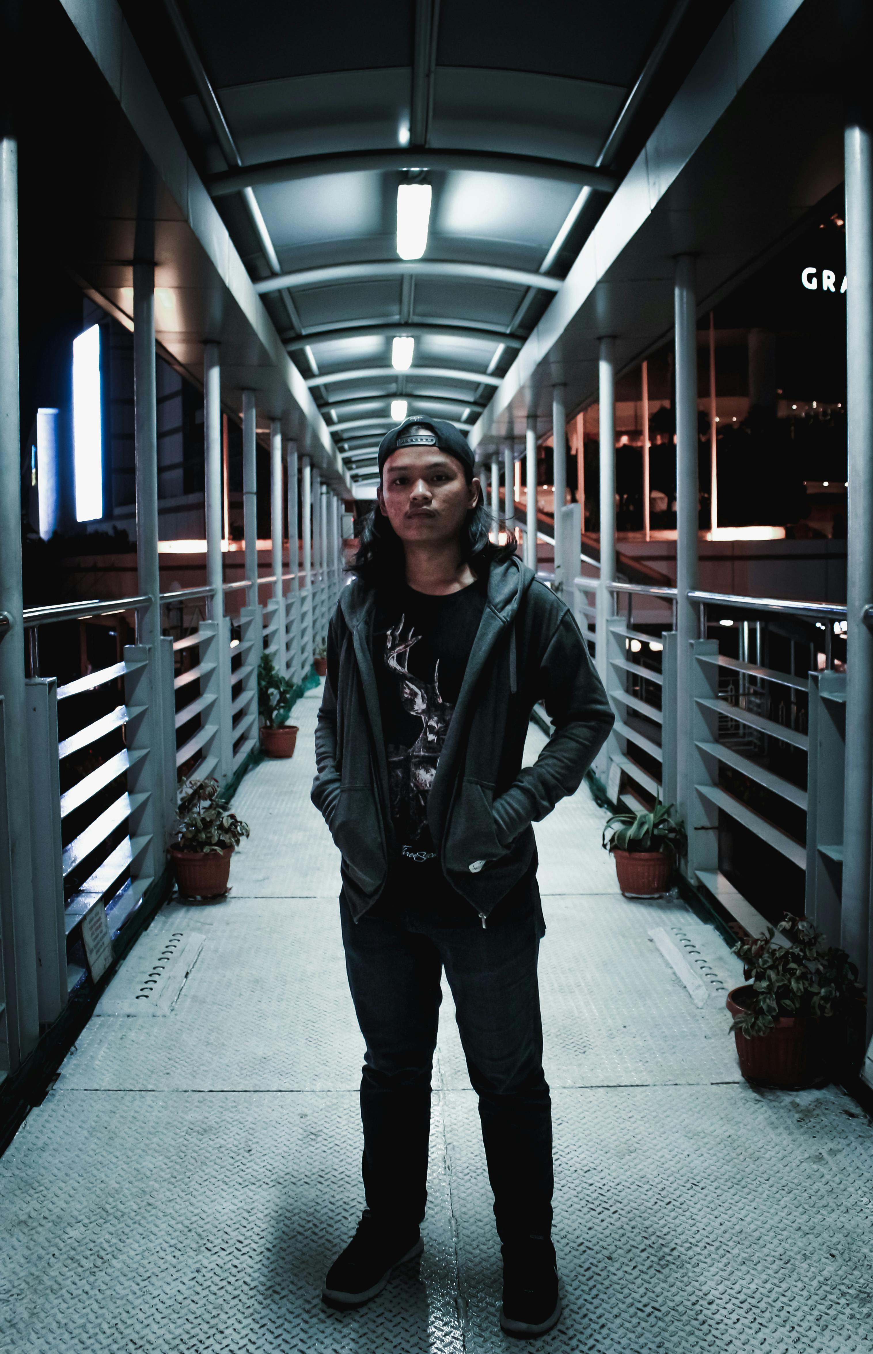 夜晚，一名年轻人自信地站在城市人行桥上，明亮的灯光映照出他的现代街头风格