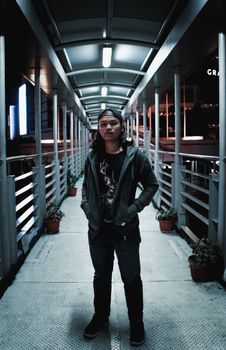 夜晚，一名年轻人自信地站在城市人行桥上，明亮的灯光映照出他的现代街头风格