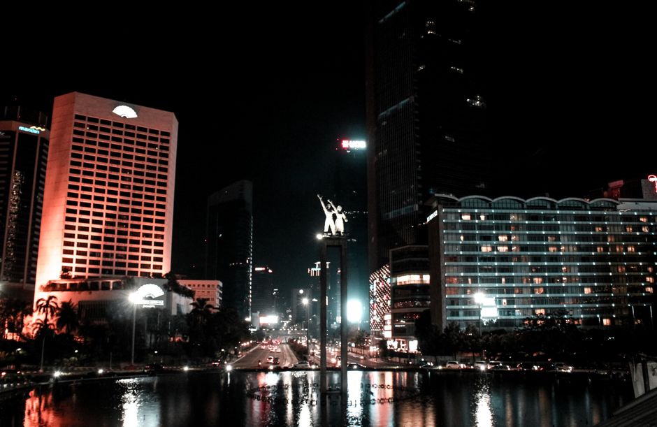 From below of illuminated Selamat Datang Monument located in downtown of Jakarta near modern buildings at night