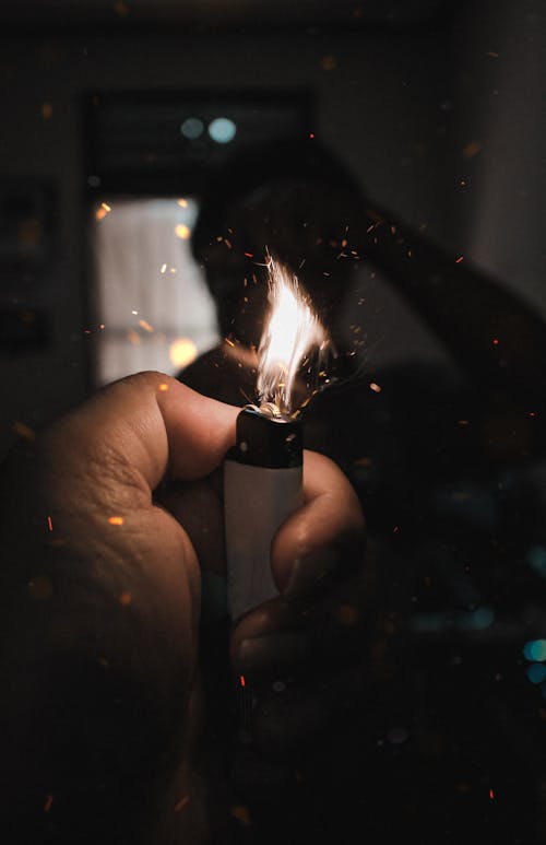 Unrecognizable male taking mirror selfie while standing in dark room with burning lighter in hand