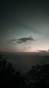 Silhouette of trees growing on mountain slope in peaceful valley against cloudy sundown sky