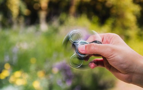 Free Close-up of a hand spinning a fidget spinner outdoors with a blurred natural background. Stock Photo