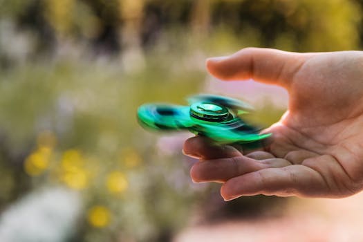 A person's hand skillfully spinning a green fidget spinner outdoors.