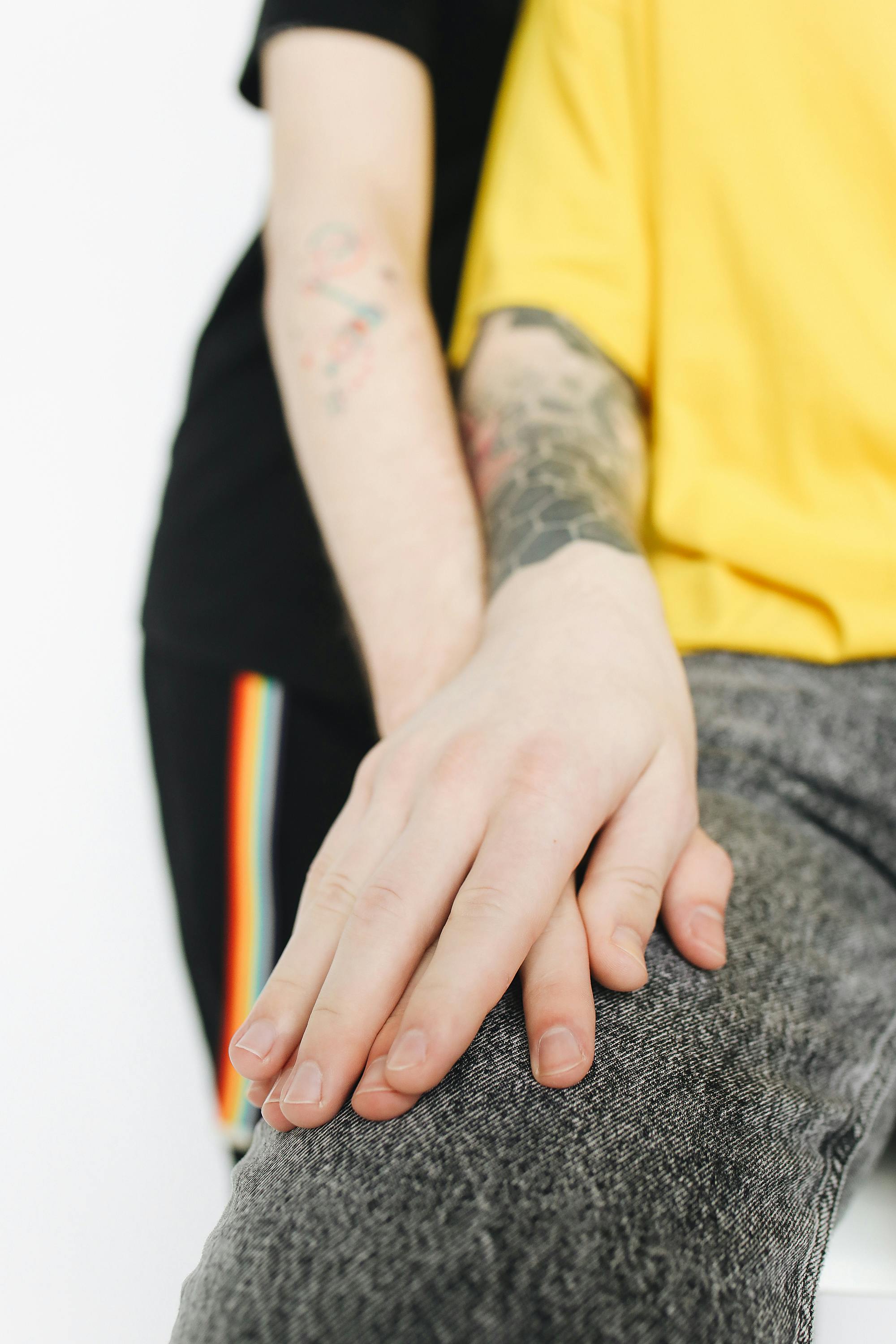 一张特写照片中，一只纹身的手搭在另一人的大腿上，展现了人际关系与休闲时尚