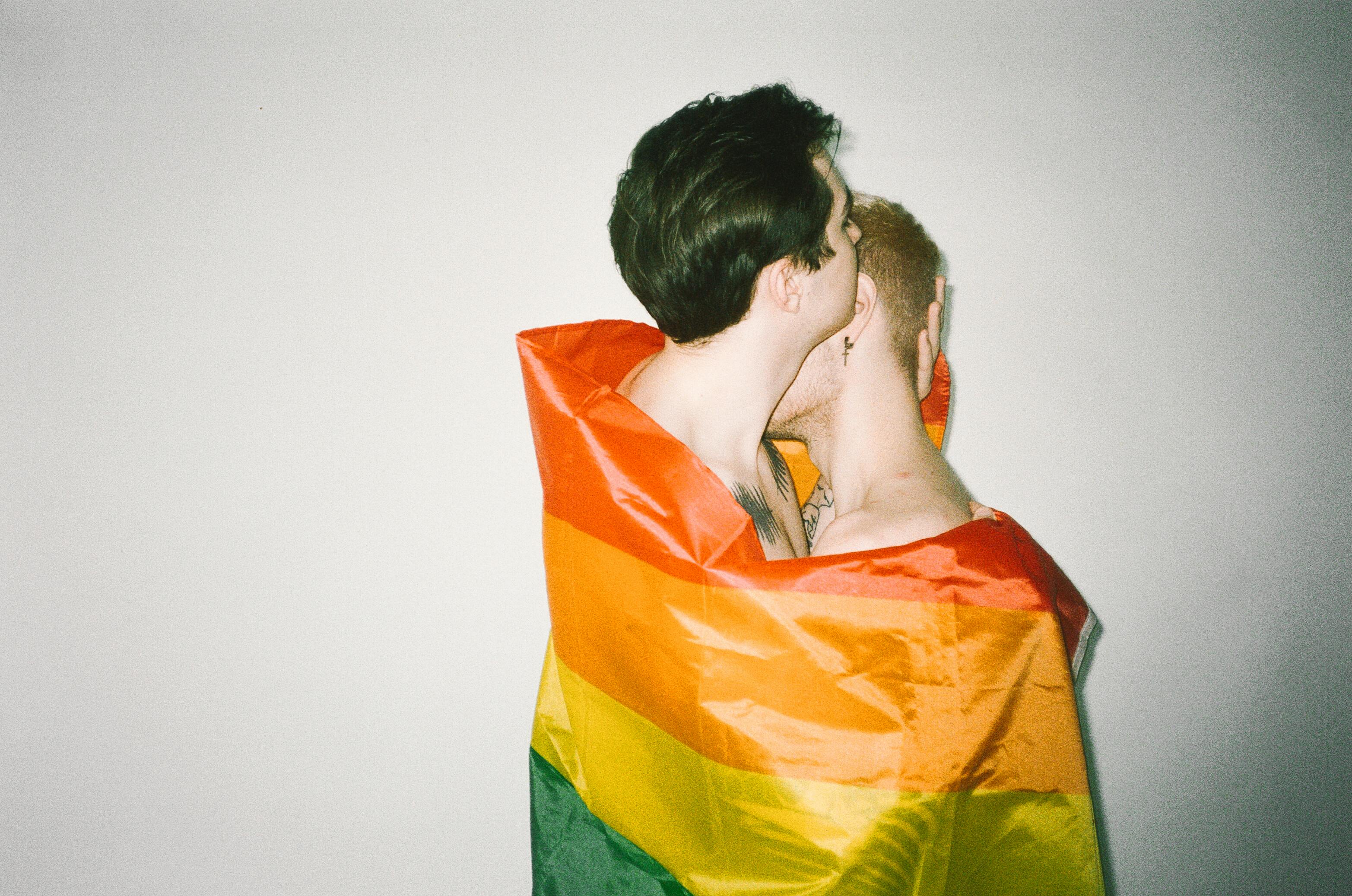 men hugging each other while covered with rainbow flag