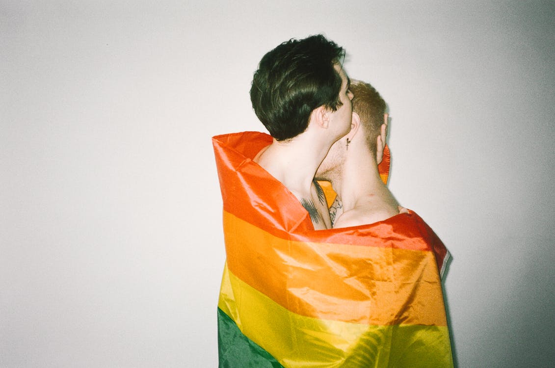 Men Hugging Each Other while Covered with Rainbow Flag 