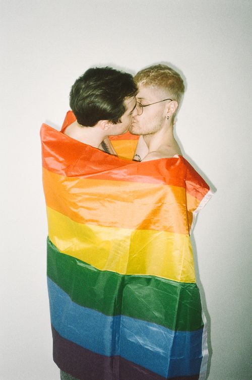 Free A loving embrace between a couple wrapped in a vibrant rainbow flag, symbolizing pride and unity. Stock Photo