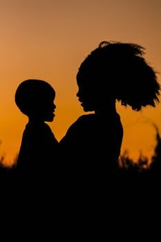 Silhouette of a mother and child in Tanzania set against a dramatic orange sunset.