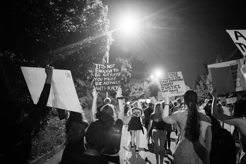 Back view of black and white crowd of unrecognizable protesting people walking on street with banners during anti racism demonstration