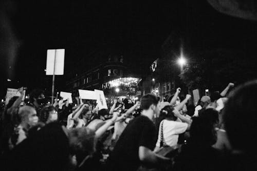 Free Side view of black and white anonymous aggressive demonstrators with fists up during protest on street at night Stock Photo