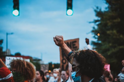 Free Side view of crop anonymous male activist with curly hair in face mask raising fist during protest on city street Stock Photo