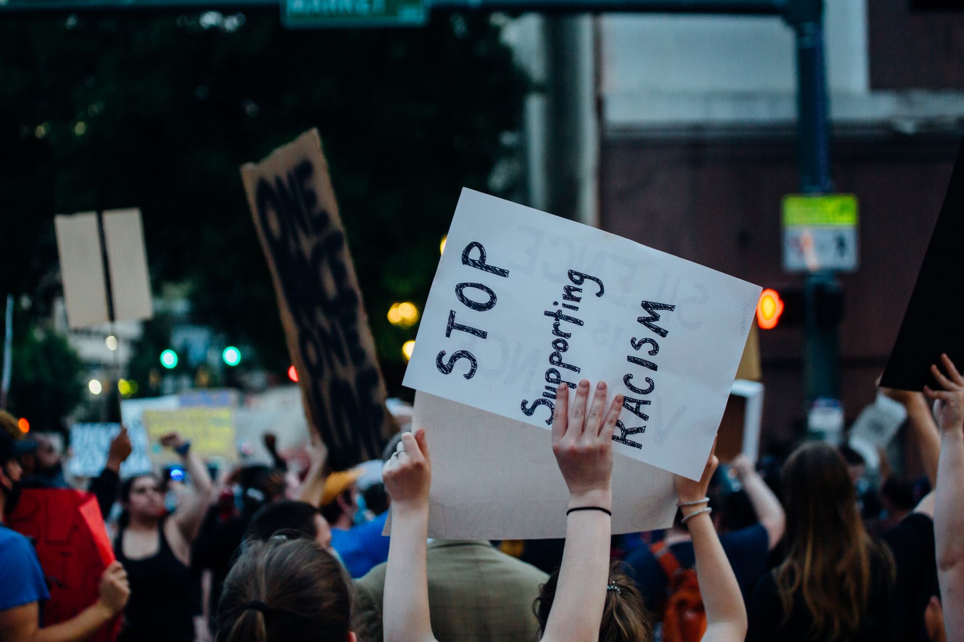 Crop unrecognizable protesters with stop supporting racism placard during demonstration on street with crowd of people