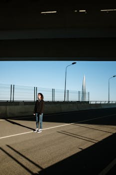 蔚蓝的天空下，现代城市建筑的映衬中，一位孤独的女人站在空荡荡的城市道路上