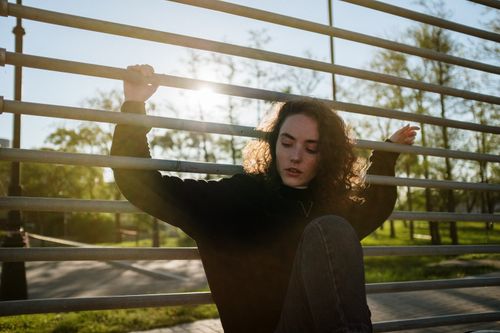 Free A young woman with curly hair relaxes against a fence in an urban park during daylight. Stock Photo