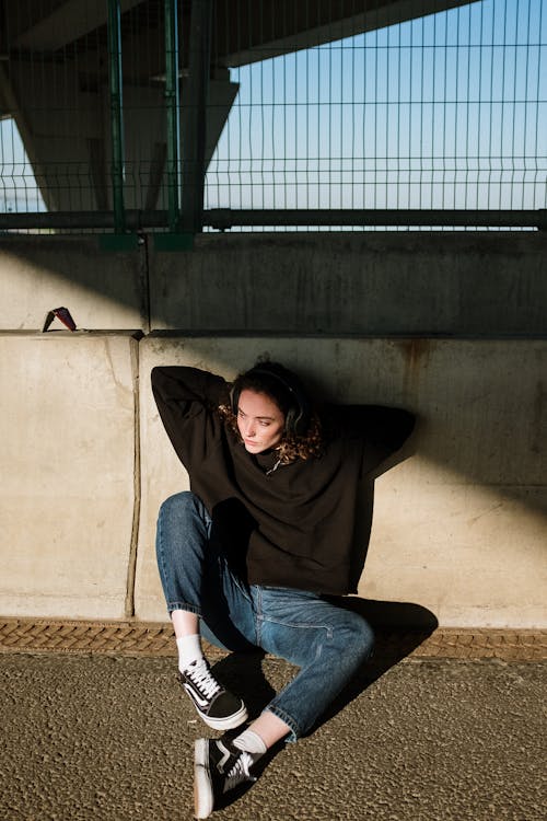 Woman in Black Long Sleeve Shirt and Blue Denim Jeans Sitting on Brown Concrete Wall during