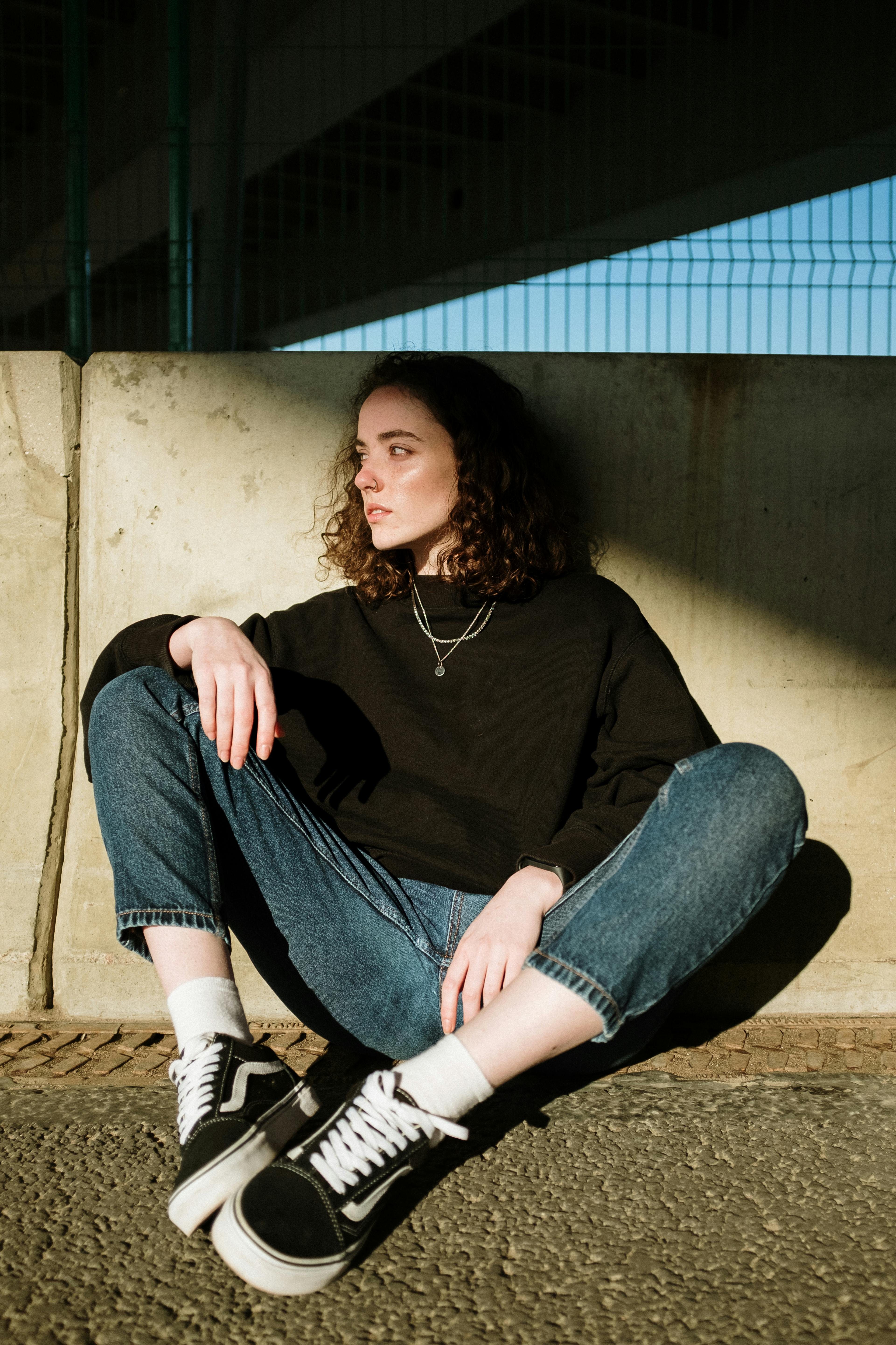 woman in black long sleeve shirt and blue denim jeans sitting on brown wooden bench