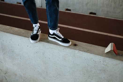 Close-up of legs in jeans and sneakers balancing on a concrete barrier in an urban setting.