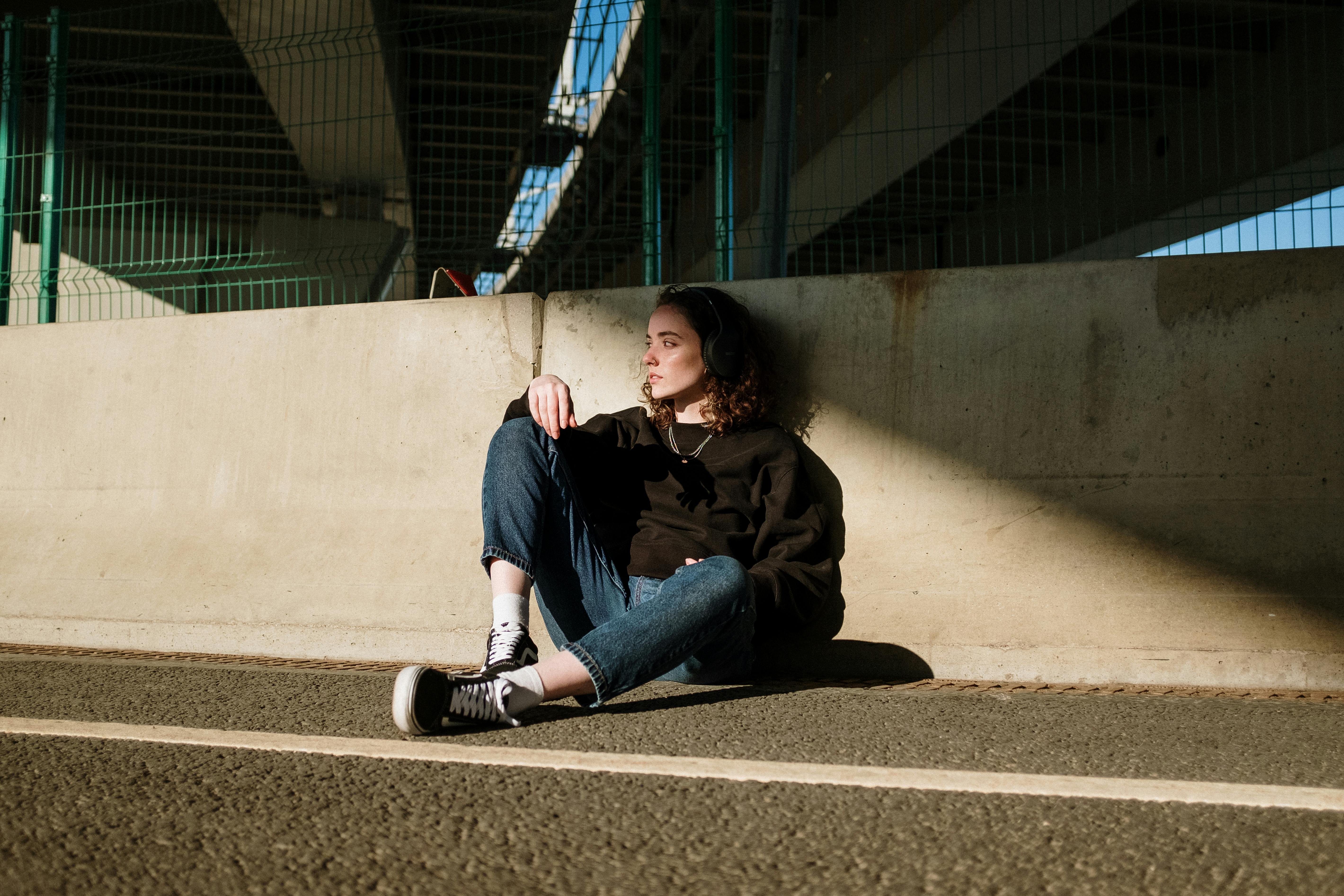 woman in black jacket and blue denim jeans sitting on gray concrete floor